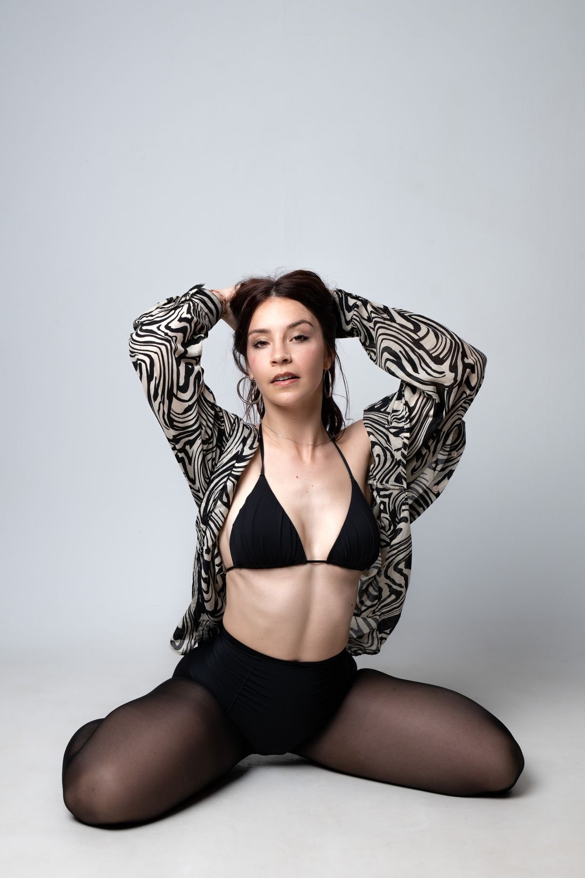 Sentada en el suelo con camisa estampada y brazos en alto