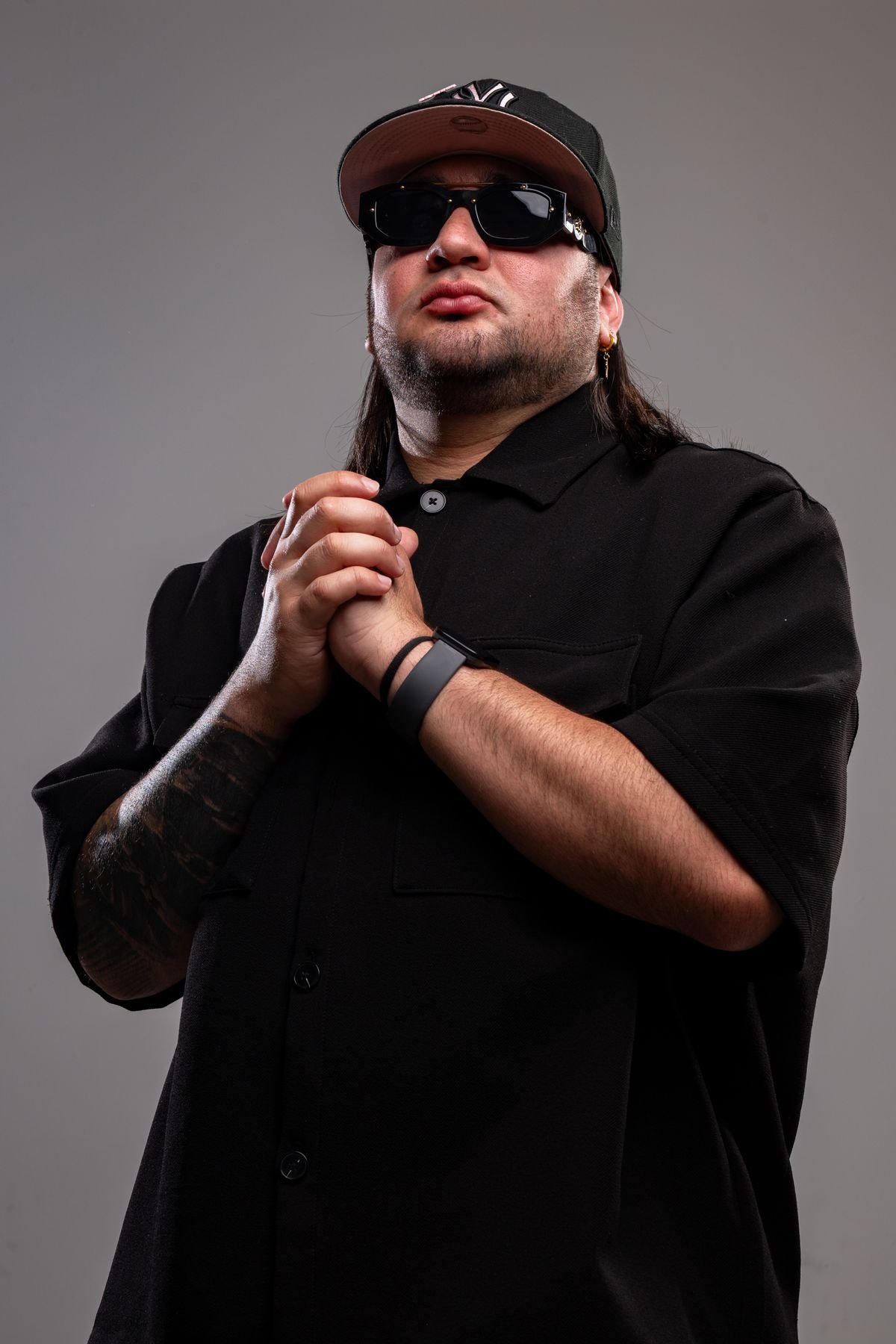 Retrato con gorra y gafas, manos juntas, fondo gris