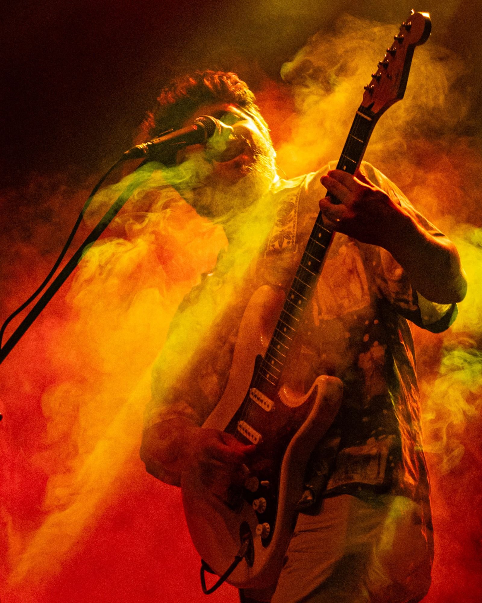 Guitarrista cantando entre humo naranja y verde