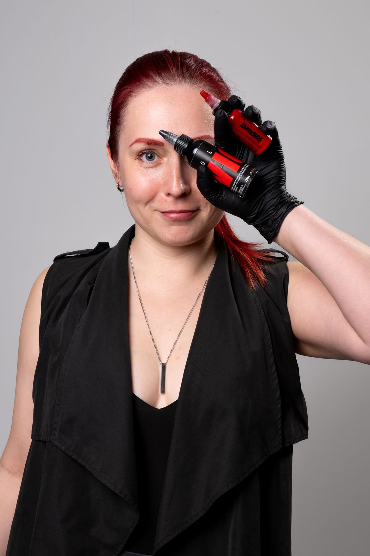 Tatuadora con frascos de tinta roja tapándose un ojo